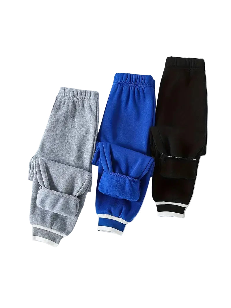 Three pairs of jogger pants in gray, blue, and black on a white surface with a shoe and headphones.