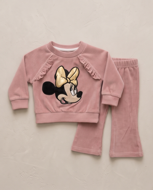 A toddler girl's two-piece corduroy pajama set in dusty pink, featuring a long-sleeve top with ruffle details and a Minnie Mouse graphic on the front, paired with matching flared pants, laid flat on a textured beige background.