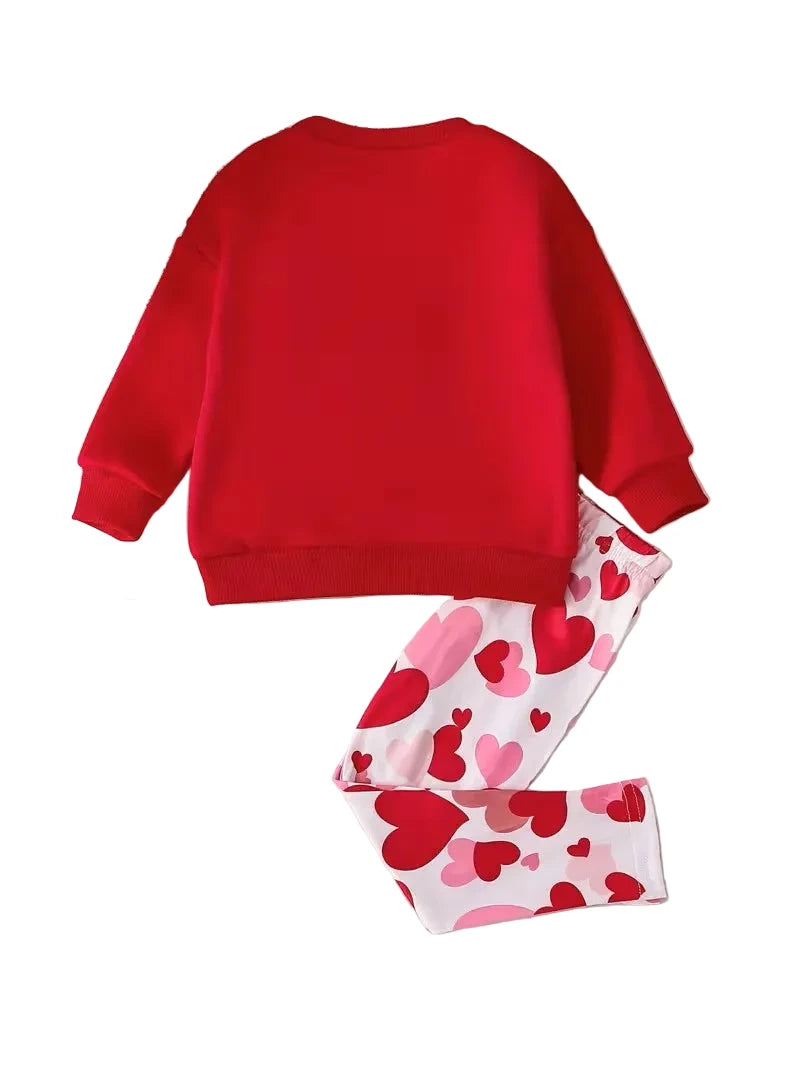 Red sweatshirt and heart-patterned pants with white shoes on a textured surface.
