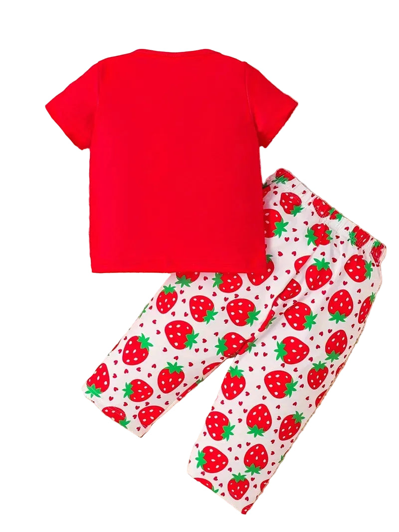 Red t-shirt and strawberry-patterned pants on a textured surface with toys around.