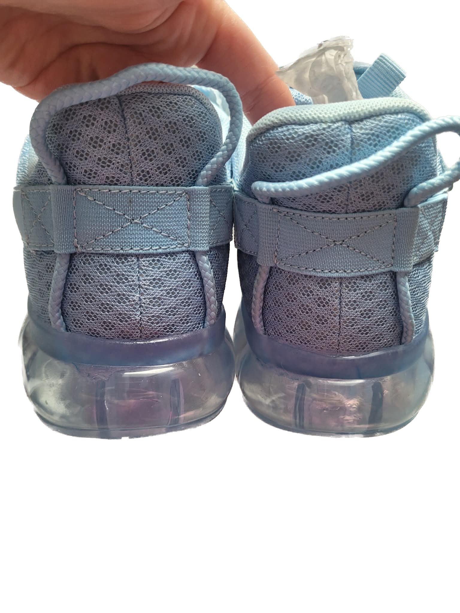 Pair of blue baby shoes held by a hand on a white background