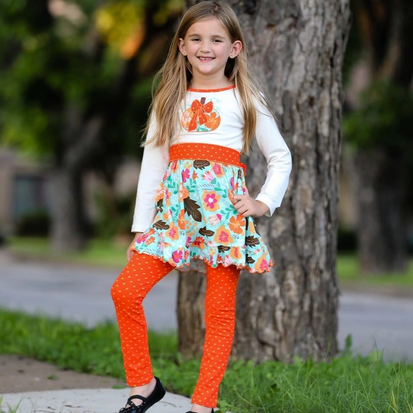 Young girl in colorful outfit standing outdoors next to a tree