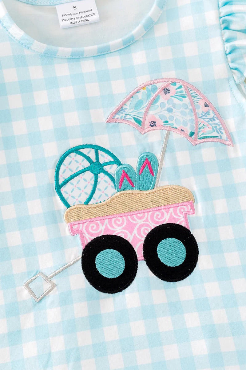 Children's outfit with a pink sandcastle and umbrella design on a blue and white checkered background.