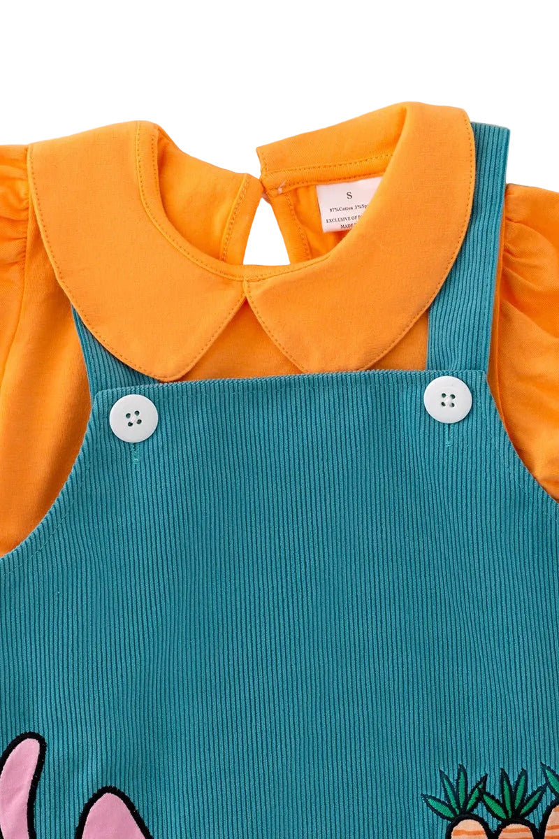 Blue corduroy pinafore dress with orange collar on a fluffy white surface