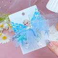 Blue decorative bow with floral elements on a card, held by a hand against a pink background with flowers.