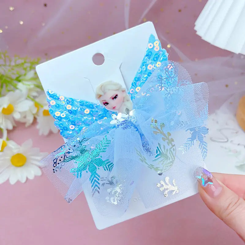 Blue decorative bow with floral elements on a card, held by a hand against a pink background with flowers.