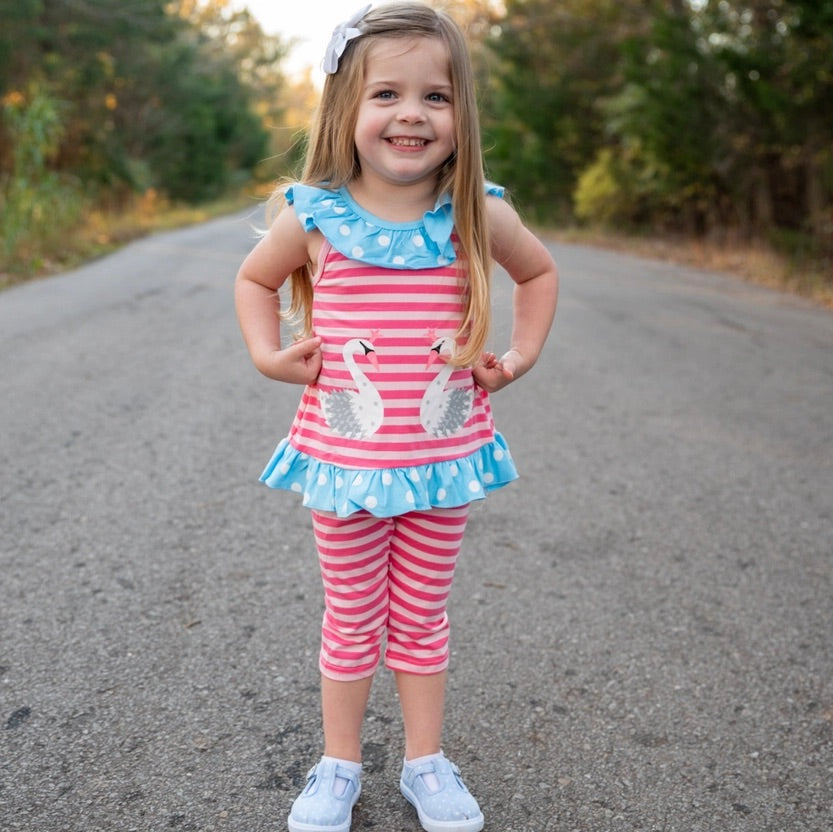 Young girl in a pink and blue outfit with swan design standing on a road.