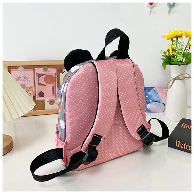 Pink polka dot backpack with black straps on a light surface.