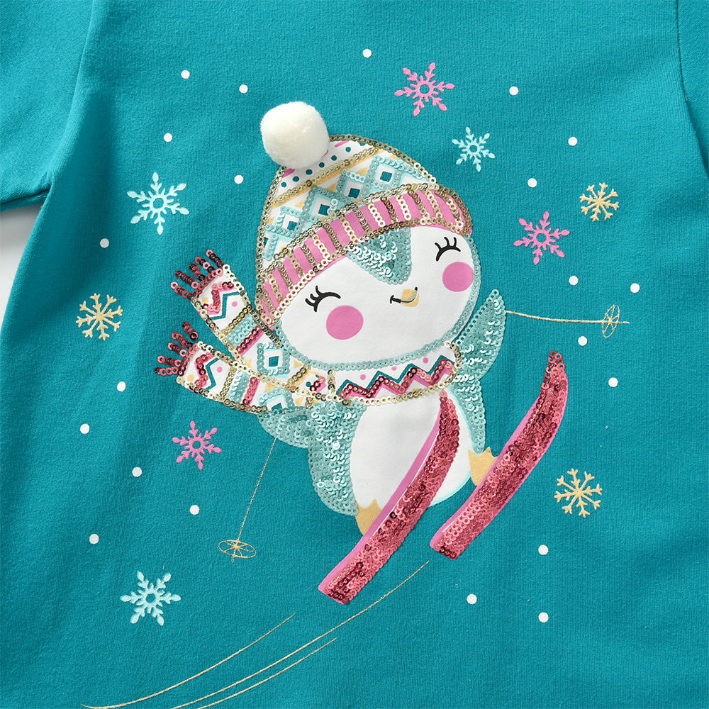 Teal shirt with a penguin design wearing a hat and skis, surrounded by snowflakes.