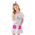 Young girl wearing a white dress with colorful butterfly designs and pink striped pockets, holding a straw.