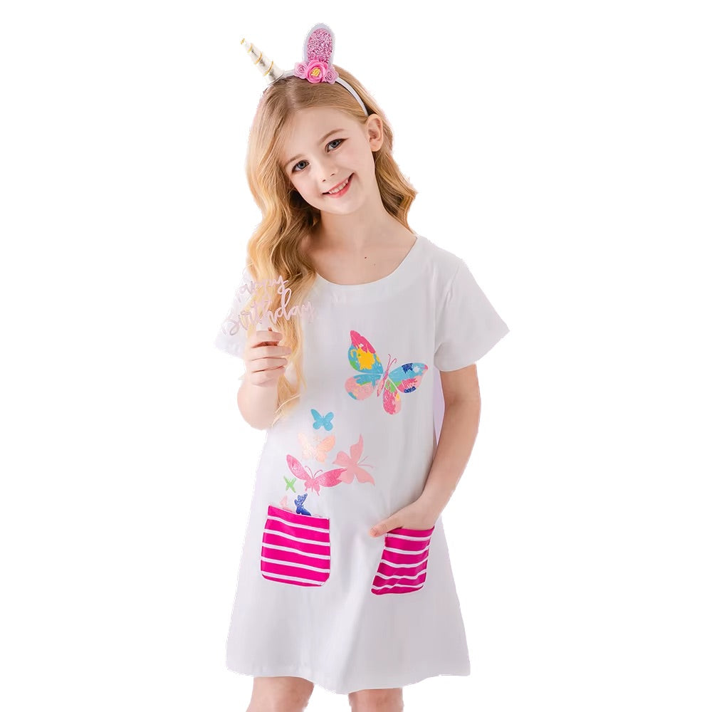 Young girl wearing a white dress with colorful butterfly designs and pink striped pockets, holding a straw.