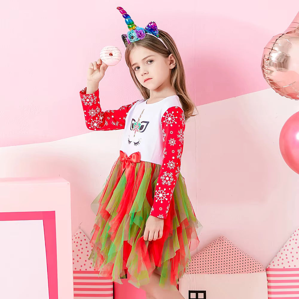 Young girl in a festive outfit with red and green dress, white shirt, and unicorn headband on a pink background.