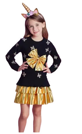Child wearing a black sweater with a large gold bow and a gold skirt, standing against a white background.