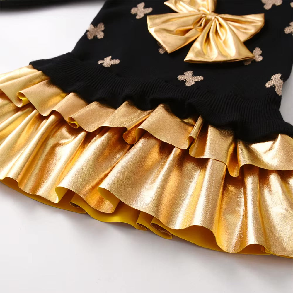 Close-up of a black top with gold bows and ruffles on a white background