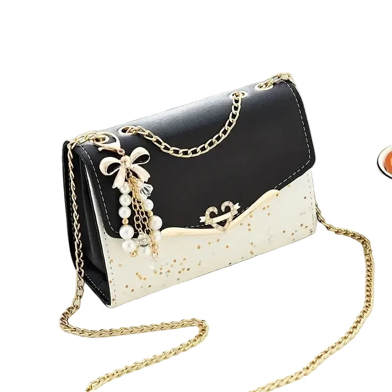 Black and white handbag with gold chain and decorative elements on a light surface.