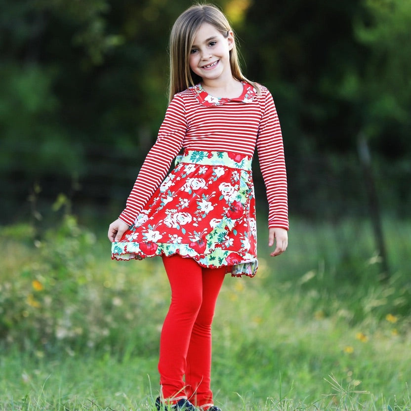 Young girl in a red and white striped dress with floral skirt standing in a grassy field.