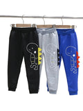 Three pairs of children's pants in black, gray, and blue with dinosaur designs on a rack.