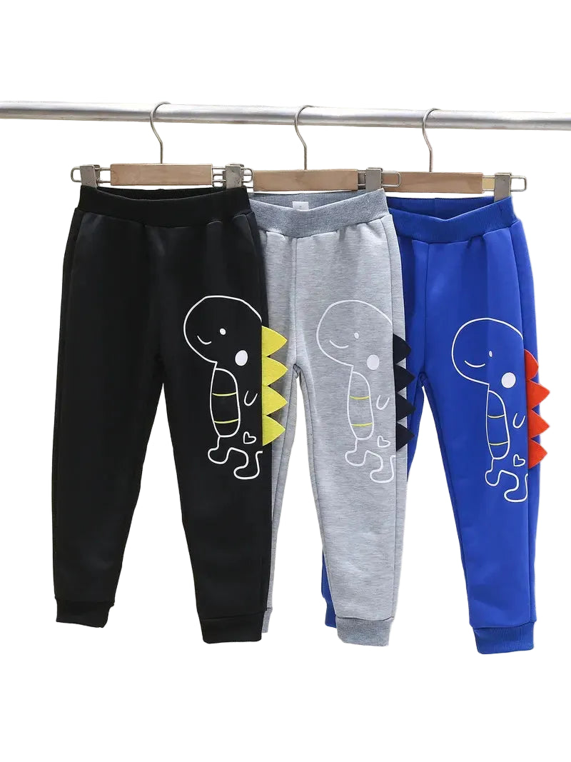 Three pairs of children's pants in black, gray, and blue with dinosaur designs on a rack.