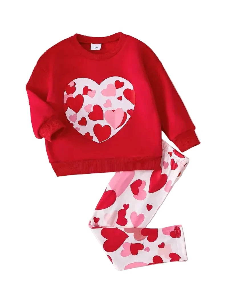 Red children's sweatshirt with heart pattern and matching pants on a wooden surface.