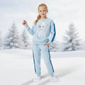 A young girl stands in a snowy outdoor setting wearing a light blue sweatshirt and matching sweatpants with dark blue side stripes and Frozen character graphics.