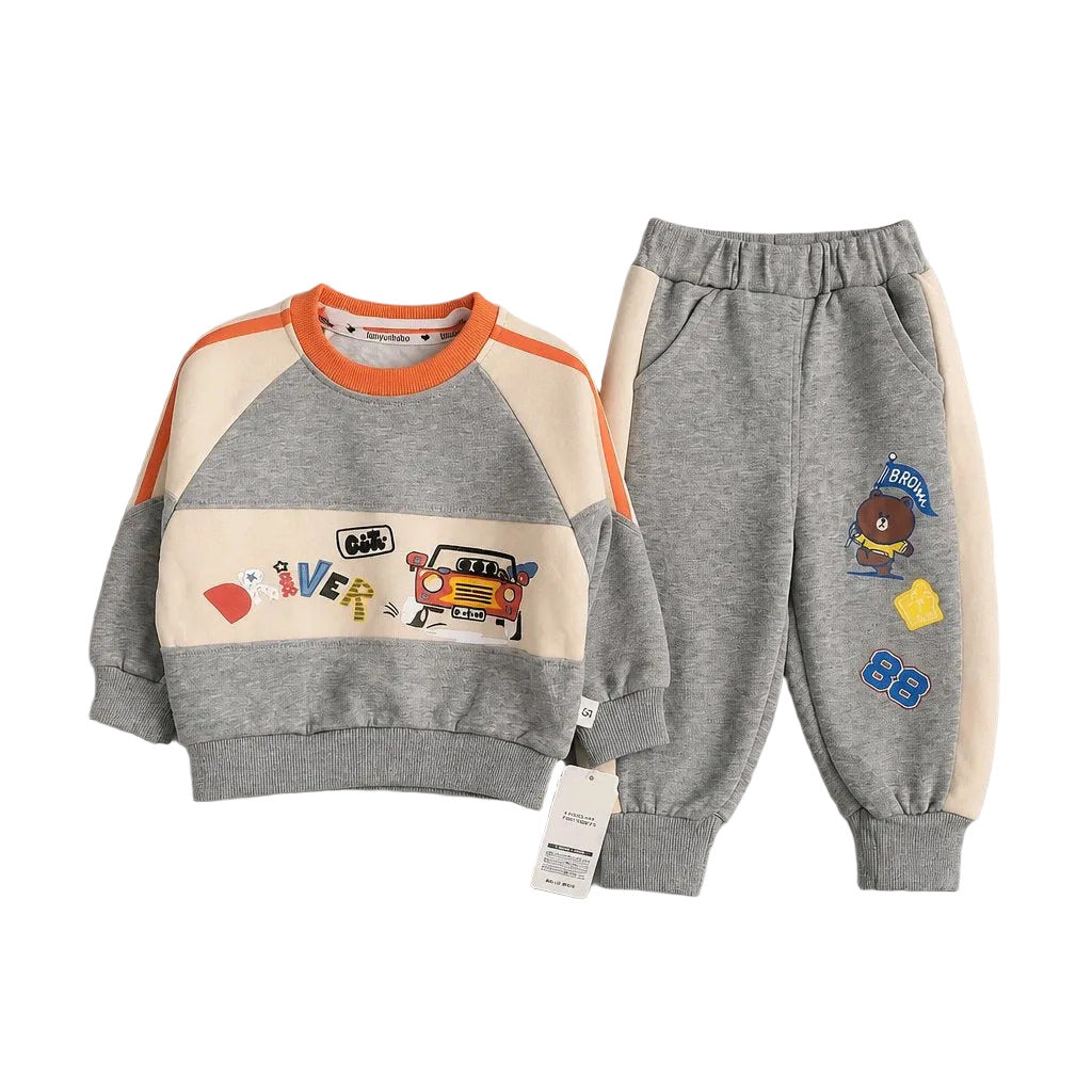 A children's two-piece sweatshirt and jogger set laid flat on a light gray background. The sweatshirt is heather gray with cream panels, orange shoulder stripes, and colorful cartoon graphics across the chest.