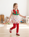 Young girl in a colorful dress with a red and green ruffled top in a room with toys.