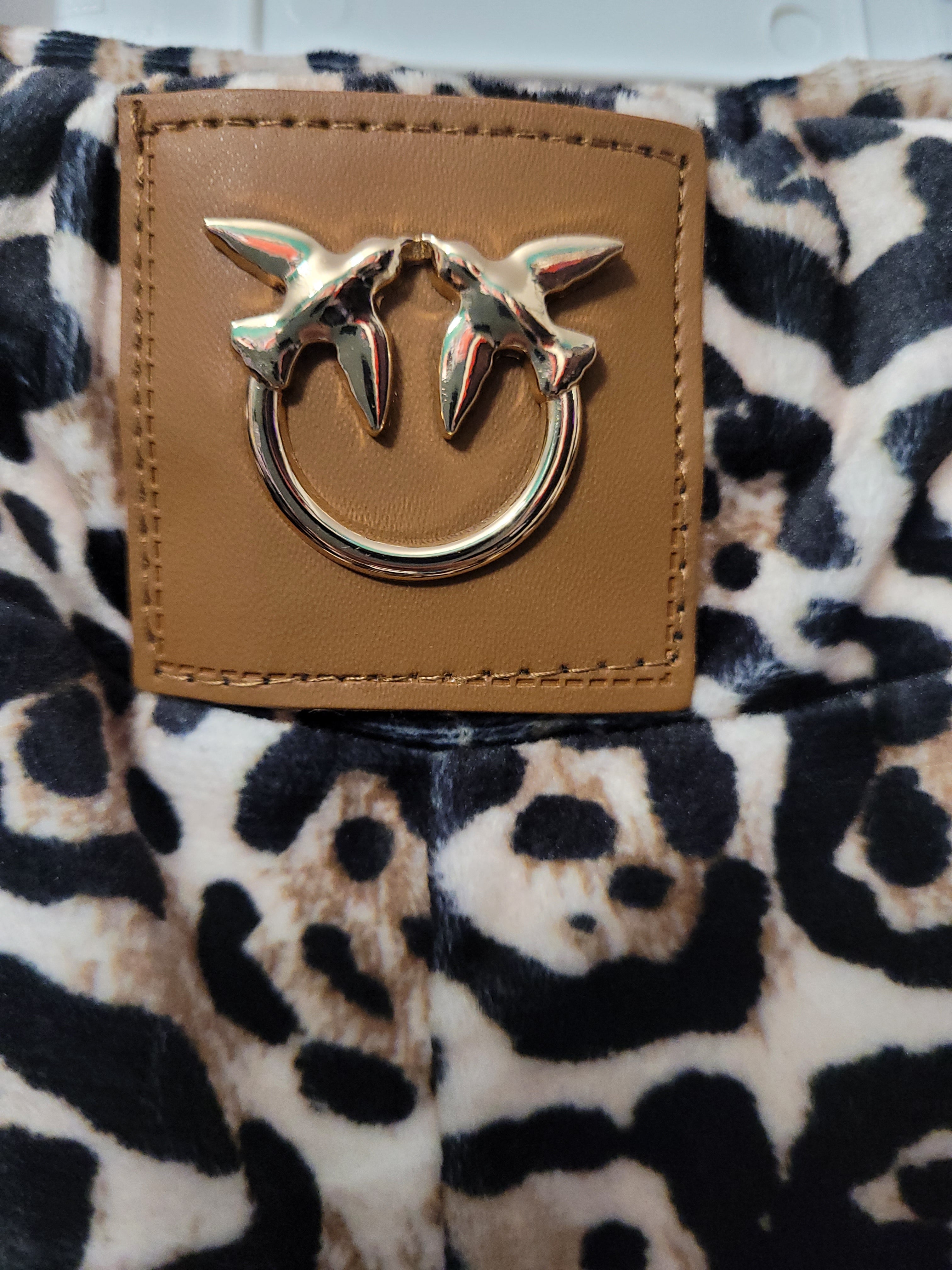 Close-up of a brown leather patch with a metal fox emblem on a leopard print fabric background.