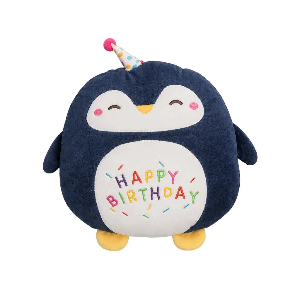 A plush penguin toy with a dark navy blue body, white belly, yellow feet and beak, and a small party hat. The belly is embroidered with 'HAPPY BIRTHDAY' in multicolored letters with sprinkle details, set against a plain light gray background.