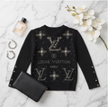 A black Louis Vuitton knit sweater with silver-tone LV logos and floral motifs embellished with rhinestones, styled in a flat lay on a white marble background with a black clutch, perfume bottle, earrings, and white orchids.