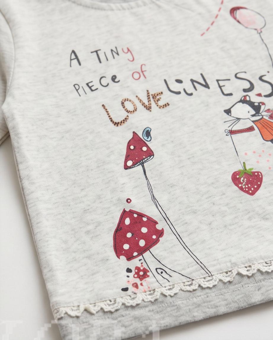 A close-up of a light gray heather baby t-shirt featuring a cute graphic print of red and white polka-dotted mushrooms, a strawberry, and the text 'A TINY PIECE of LOVE linESS'.