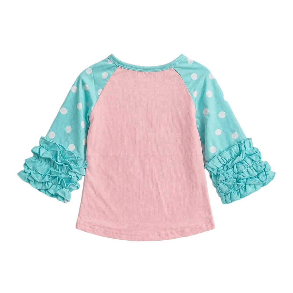 A children's raglan-style top shown from the back, featuring a light pink body, aqua blue sleeves with white polka dots, and matching aqua blue ruffled cuffs, laid flat on a light gray background.