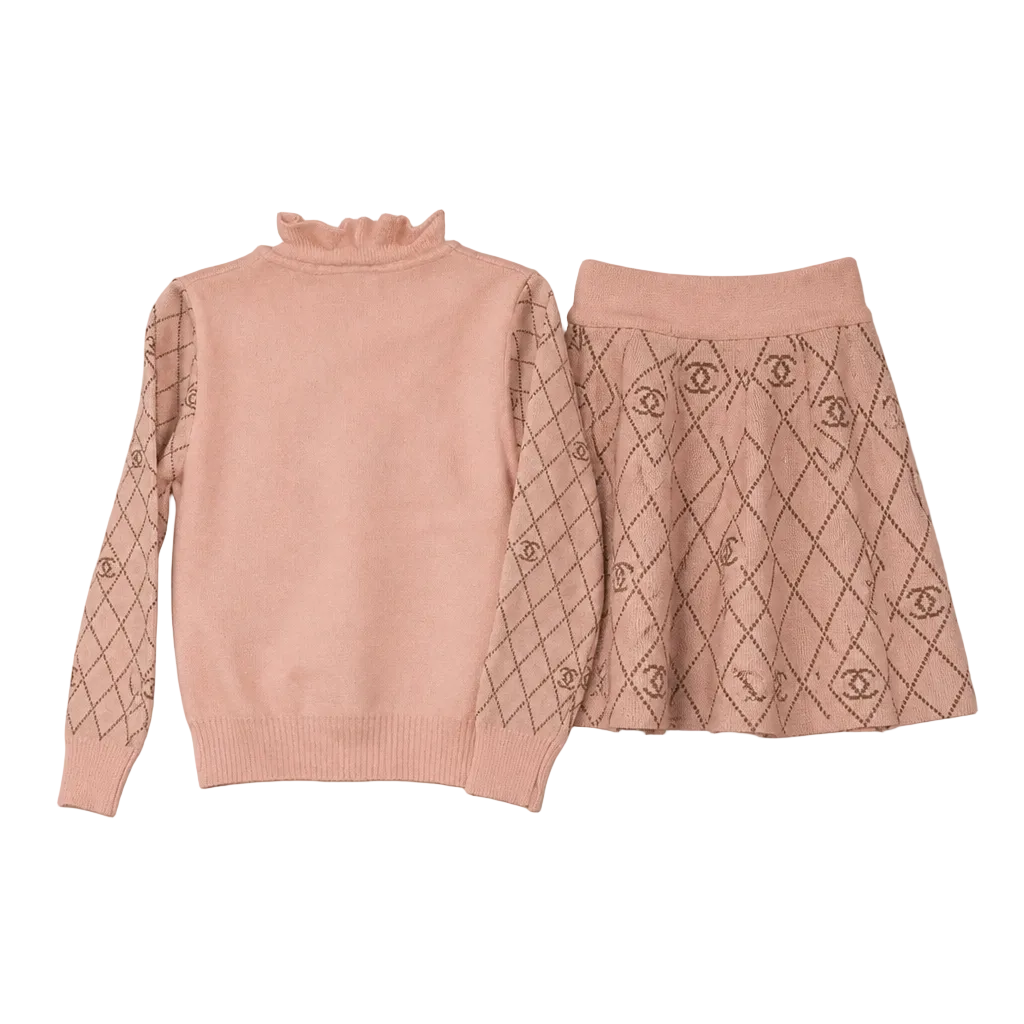 A two-piece girls' knit set in dusty pink, featuring a mock neck long-sleeve sweater with a diamond pattern on the sleeves and a matching A-line skirt with a repeating Chanel logo pattern.