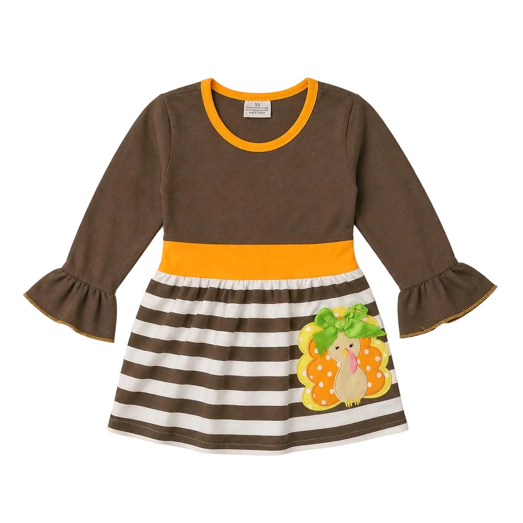 A toddler's long-sleeve dress with a solid brown top, a bright orange-yellow waistband, and a brown and white striped skirt featuring a decorative turkey and acorn applique. The sleeves have ruffled cuffs with orange trim, and the dress is shown flat against a light gray background.