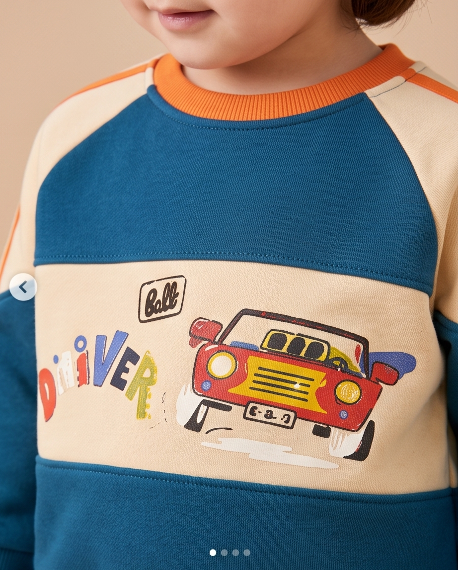 Close-up of a child wearing a colorblock raglan sweatshirt with a cartoon car and 'Baller Driver' graphic. The sweatshirt features a cream body, a teal blue lower half, and orange ribbed collar, with a red and yellow car illustration on the front.