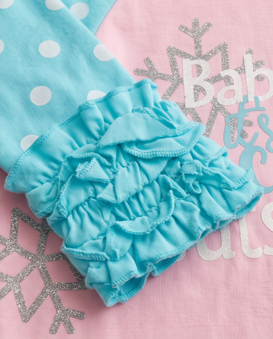 A close-up of a baby garment featuring a light blue ruffled leg warmer or diaper cover over matching light blue leggings with white polka dots, laid flat on a pink printed fabric background.