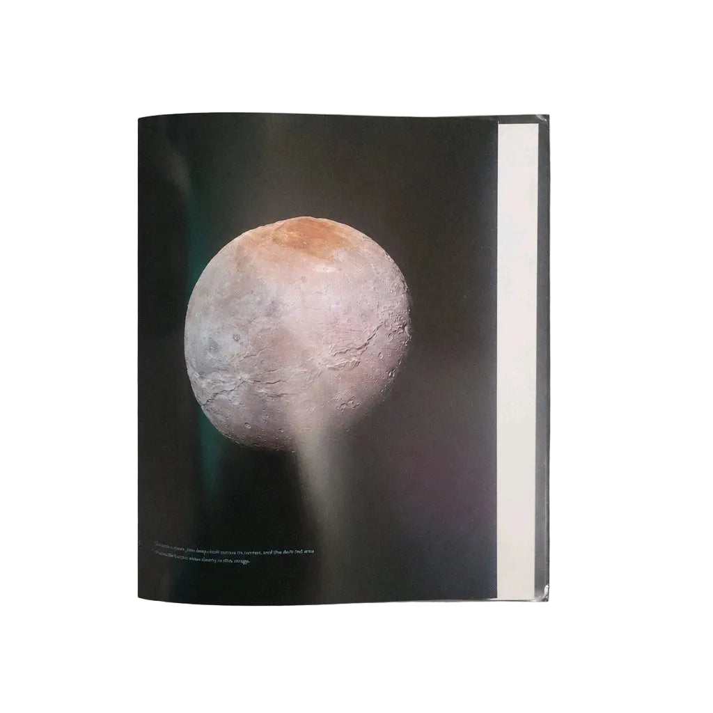A hardcover book or magazine with a black cover featuring a close-up photograph of a cratered celestial body, photographed against a light gray background.