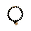 Black beaded bracelet with a gold charm on a light gray background