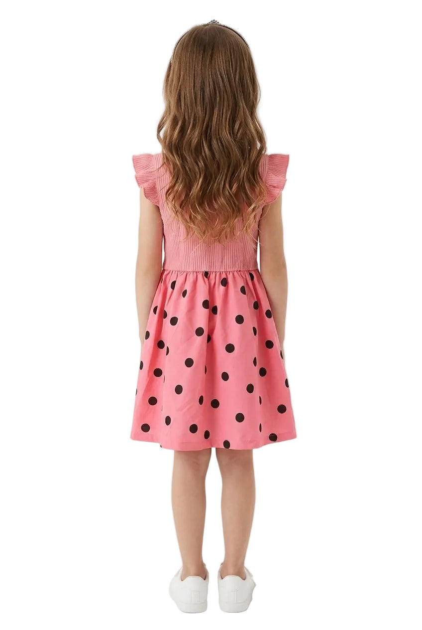 Young girl wearing a pink dress with black polka dots, standing against a white background.