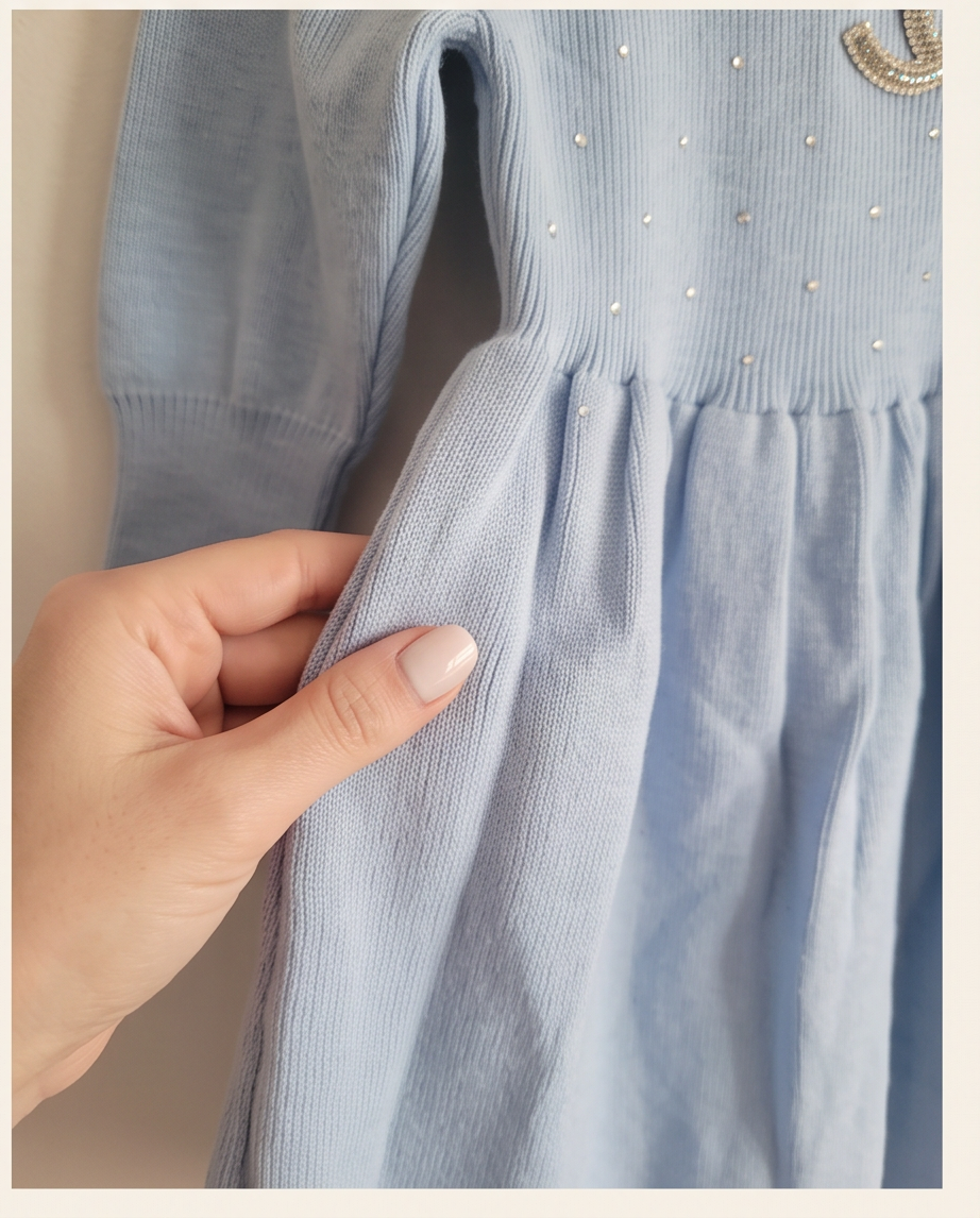 A close-up of a light blue ribbed knit dress being held by a hand, showing the texture of the fabric and small rhinestone embellishments on the bodice.
