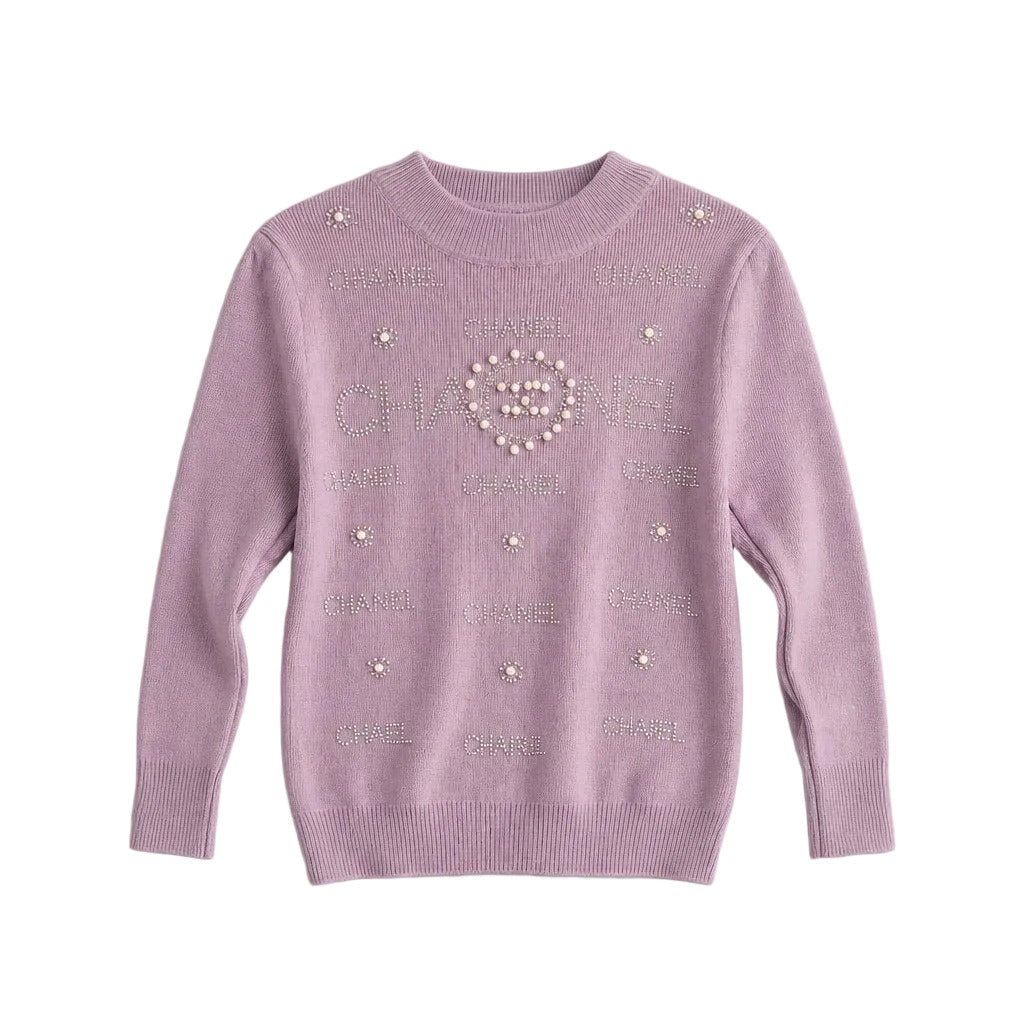 A light purple knit sweater featuring Chanel branding with rhinestones and faux pearls, displayed flat against a light gray background.