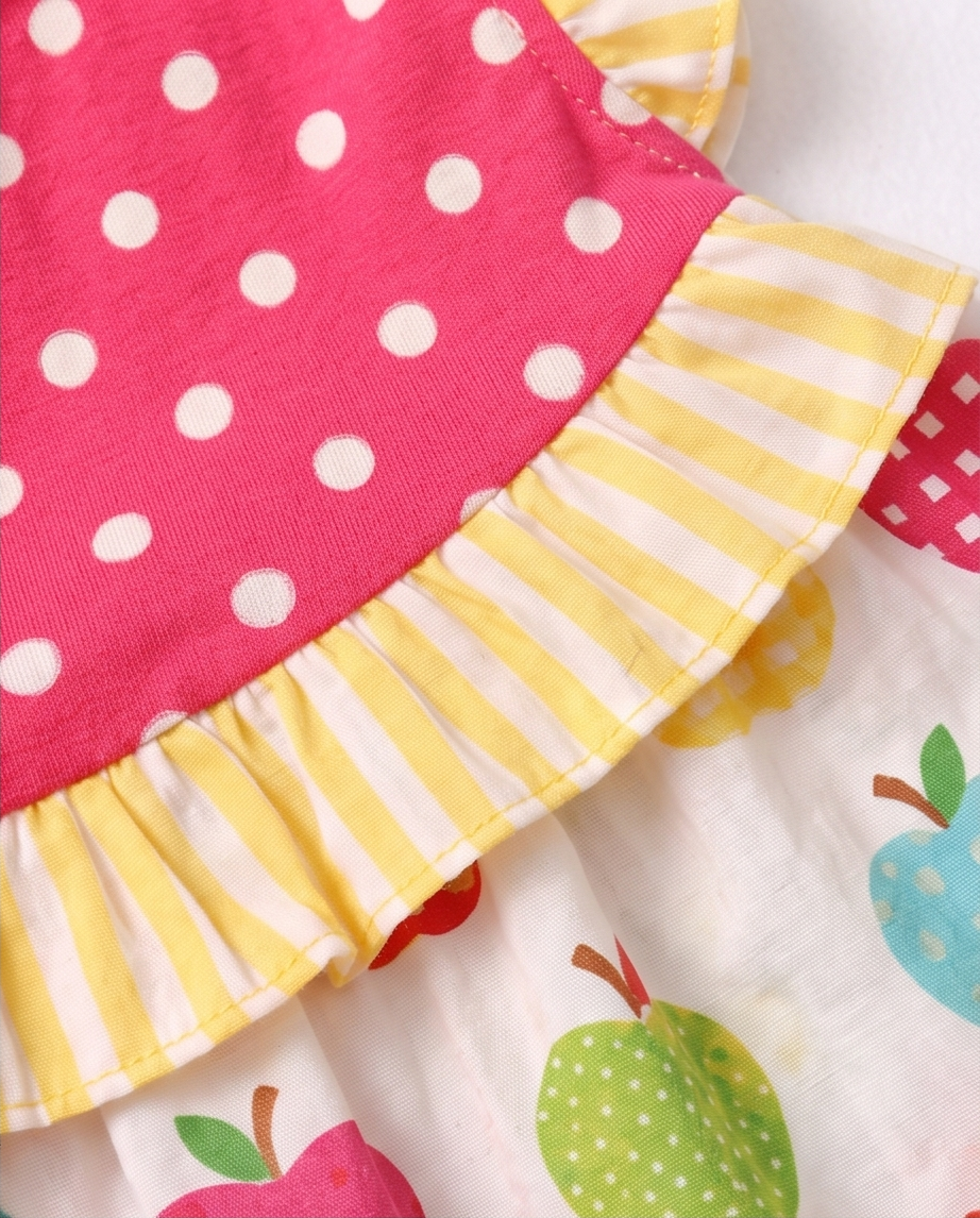 Close-up of fabric with pink polka dot and yellow striped border, featuring colorful apple pattern.