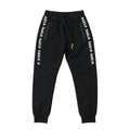 Black sweatpants with white 'KAER KAEIR' text printed down both sides of the legs, featuring a drawstring waist and zippered side pockets, shown flat on a light gray background.
