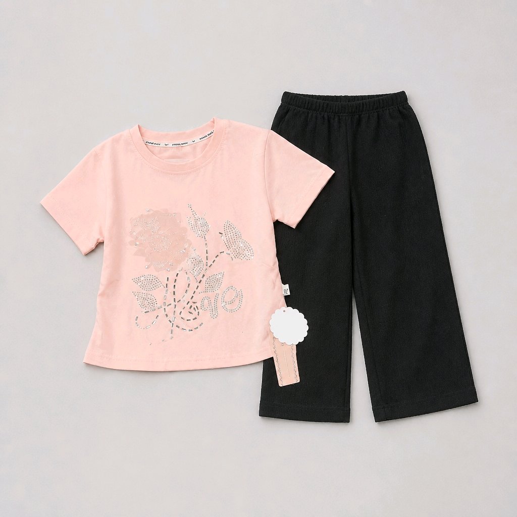 A children's two-piece outfit set featuring a light pink short-sleeve t-shirt with a rhinestone-embellished floral design on the front, paired with black wide-leg cropped pants, laid flat on a neutral gray background.