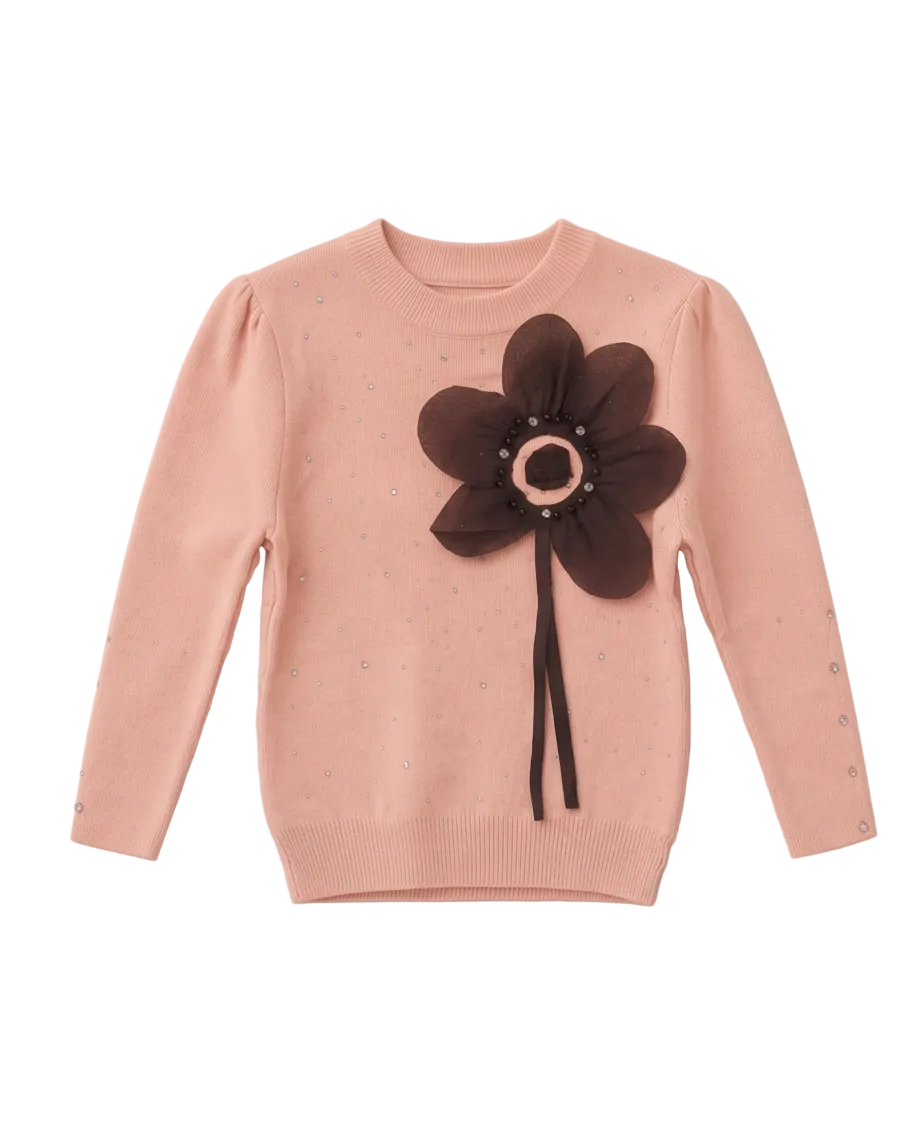 A light pink knit sweater with a large dark brown fabric flower applique on the chest, featuring a circular metallic center and a long dark ribbon stem, laid flat on a neutral light gray background.