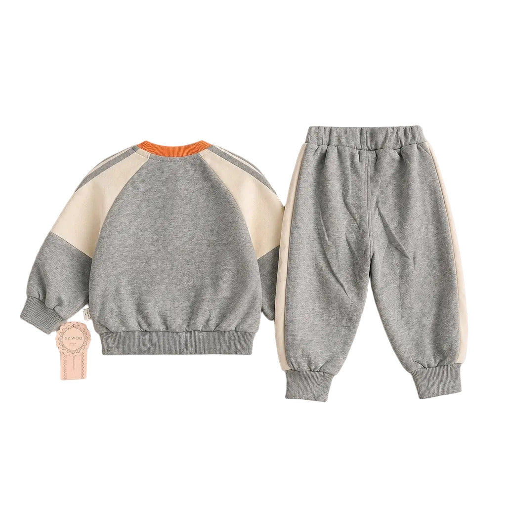 A children's two-piece sweatshirt and jogger set laid flat on a light gray background. The sweatshirt is heather gray with cream panels on the shoulders and sleeves, plus a bright orange collar.
