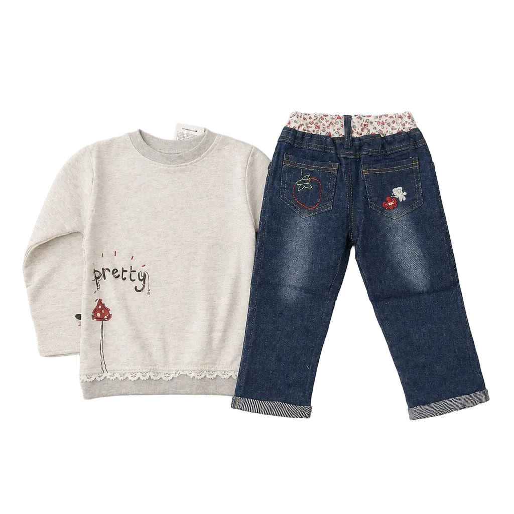 A children's two-piece outfit laid flat on a light gray background, featuring a heather cream long-sleeve top with 'pretty' embroidered on the front and blue denim pants with floral-patterned waistband and embroidered red mushroom details on the back pockets.