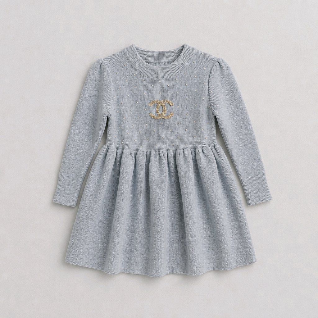 A light gray knit long-sleeve dress for toddlers, featuring a gathered waist and a gold embroidered interlocking CC logo on the chest, displayed against a neutral light gray background.
