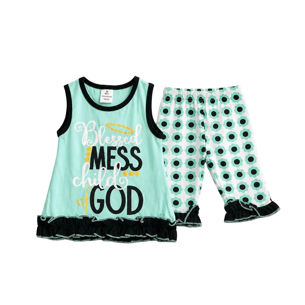 A two-piece baby girl's outfit set featuring a mint green sleeveless tank top with black trim, black text reading 'Blessed Mess child GOD', and a black ruffle hem, paired with matching mint green and black polka dot pants with black ruffle hems, laid flat on a neutral gray background.