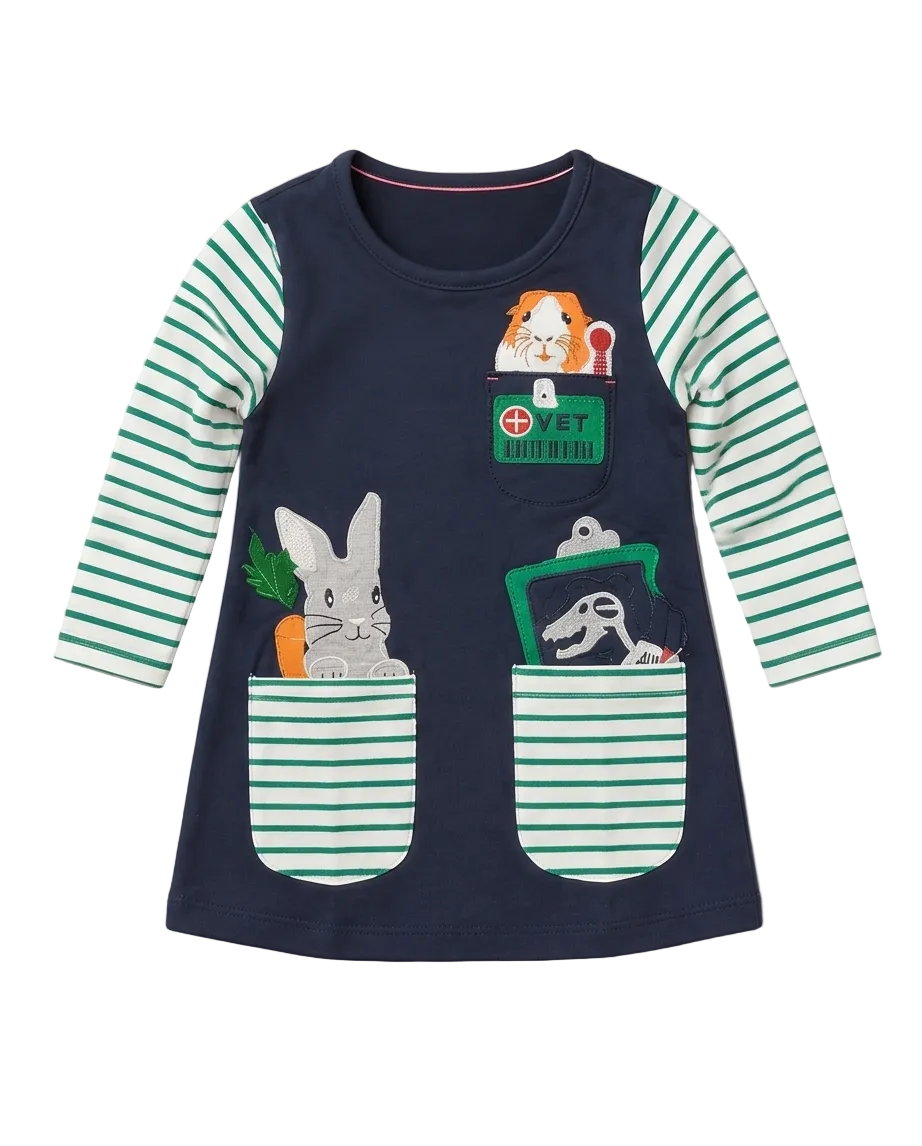 A toddler girl's long-sleeve tunic dress in navy blue with mint green and white striped sleeves and pockets. The front features cartoon animal graphics peeking out of the pockets, including a rabbit, a guinea pig, and a dinosaur, with a green 'VET uniform' patch detail on the chest.