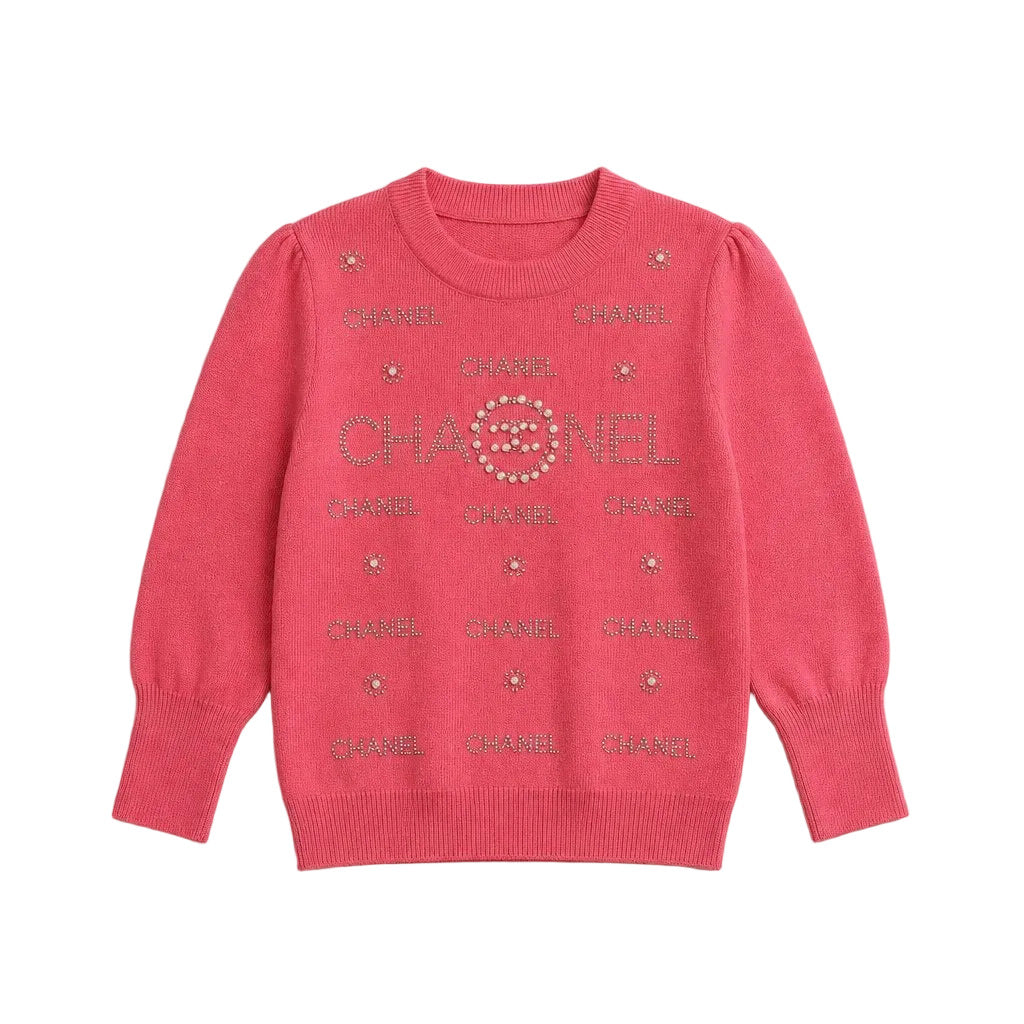A pink knit sweater featuring 'CHANEL' text and rhinestone star motifs printed across the front, laid flat on a neutral light gray background.